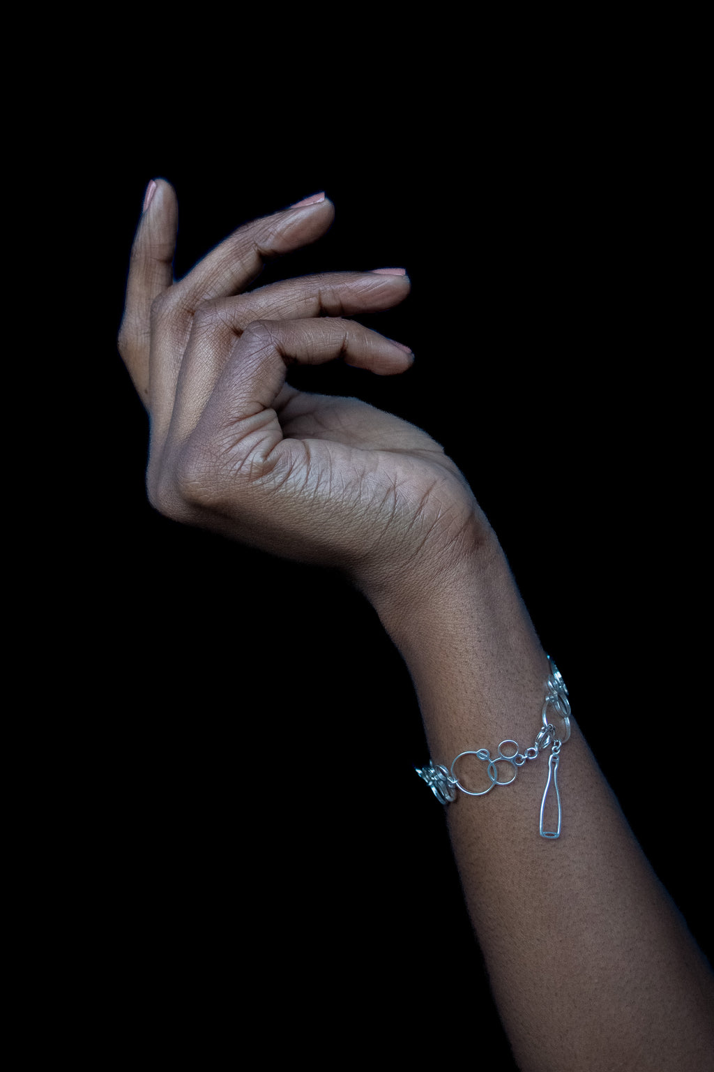 Hand wearing a silver charm bracelet on a black background