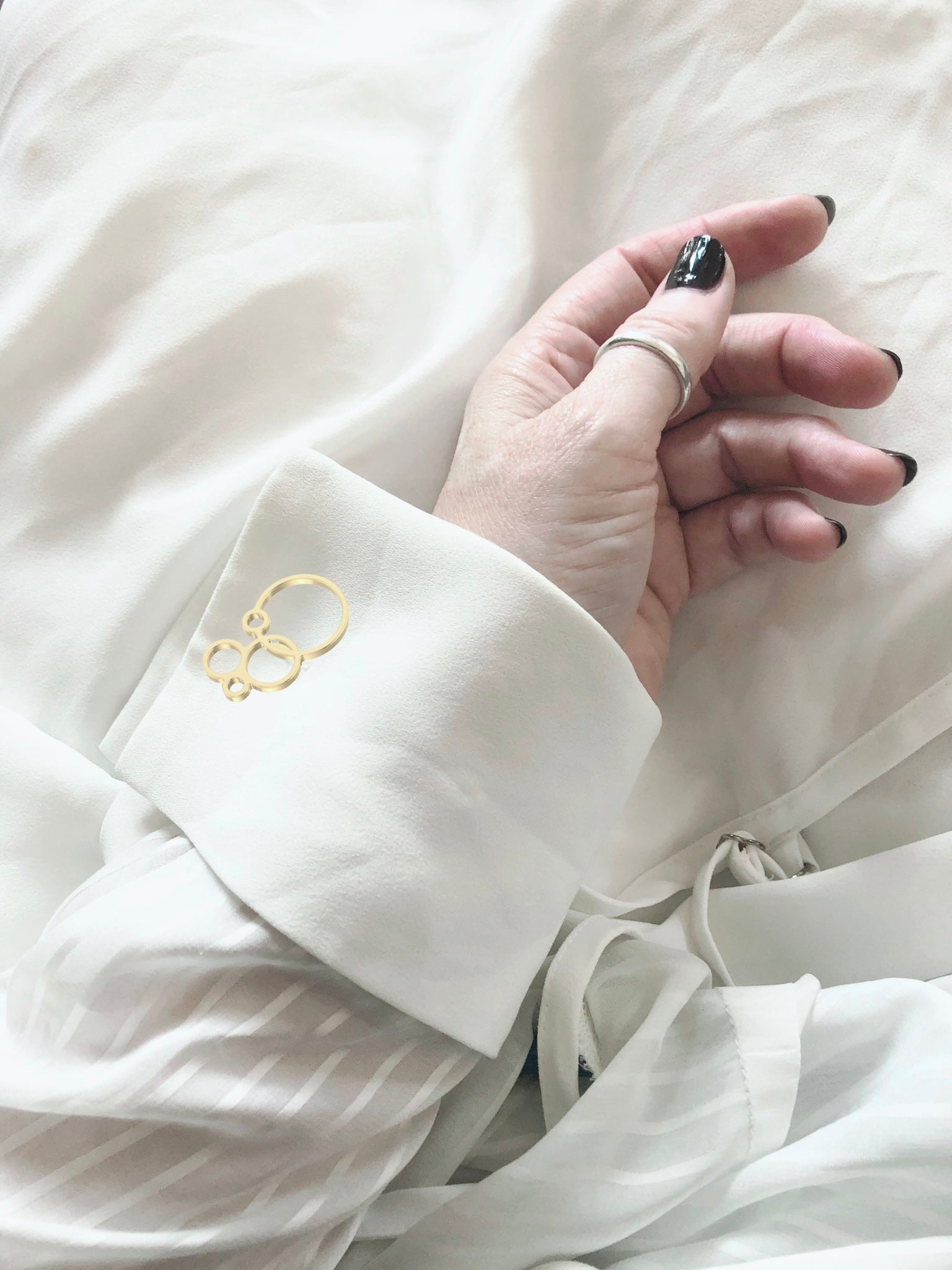 White shirt with gold bubble cufflink worn by a person with black nail polish.