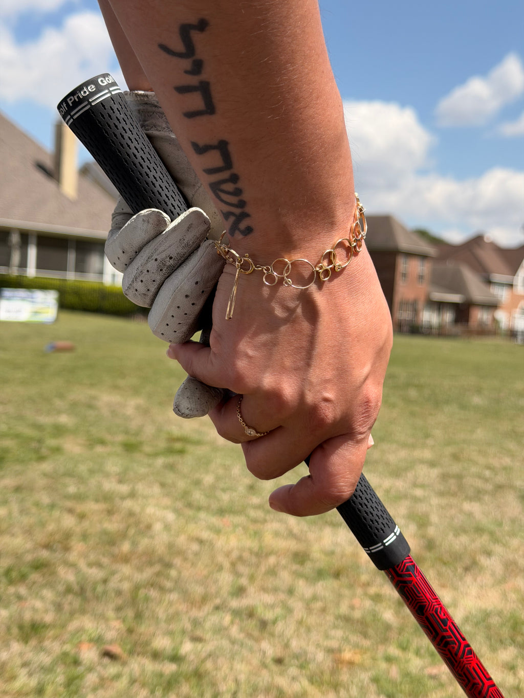 Hand holding golf clubs with a gold charm bracelet on a golf course